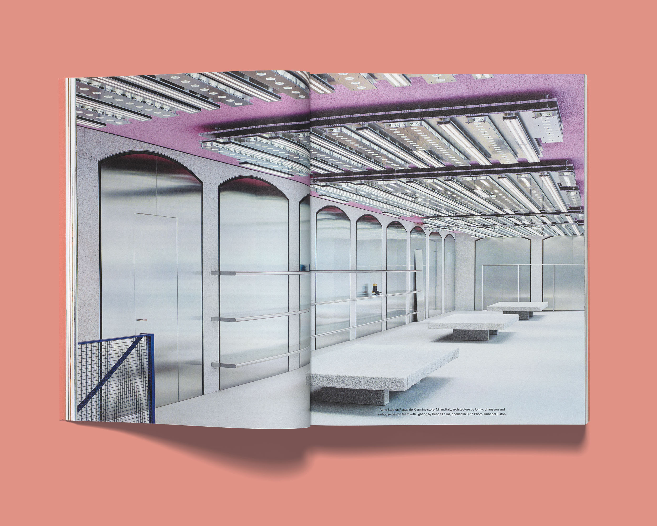 Open Acne Paper spread showing the interior of the Acne Paper Piazza del Carmine store in Milan, set against a coral-pink background.